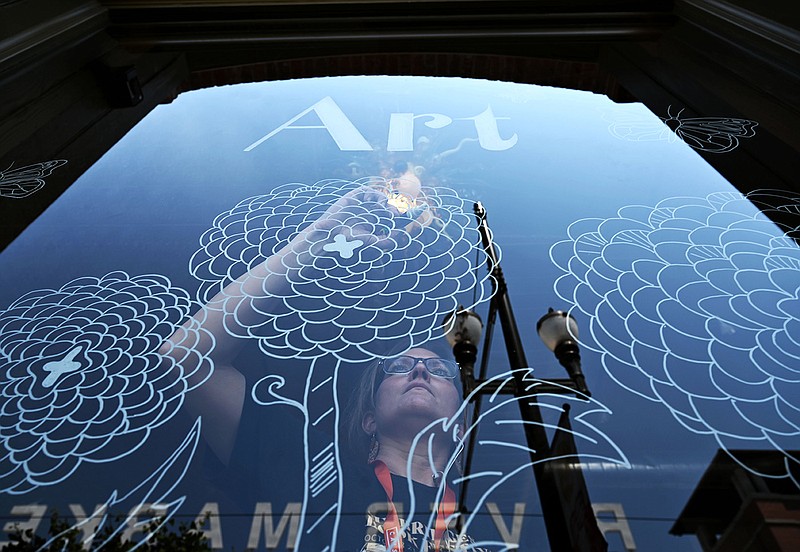 Elizabeth Rogers paints on the window of the Galleries and Bookstore at Library Square on Thursday, May 12, 2022 in preparation for the second Friday gallery opening.

(Arkansas Democrat-Gazette/Stephen Swofford)