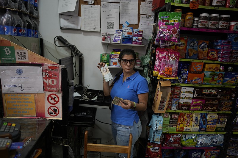 Rim Hassam holds Bolivars and U.S currency that she received from a customer as payment in her shop, in Caracas, Venezuela, Friday, May 13, 2022. A new tax law approved by the Venezuelan government, that went into effect in March, applies a 3% tax charge on transactions paid in foreign currencies. (AP Photo/Ariana Cubillos)