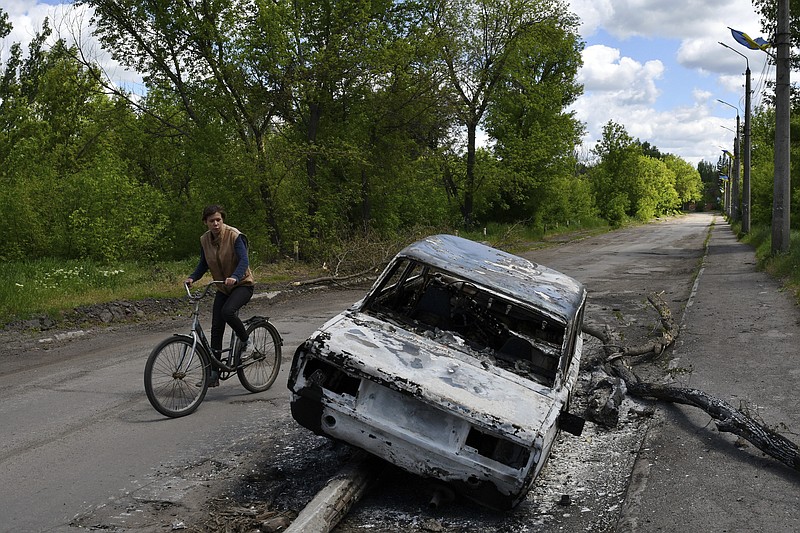 A man rides a bicycle past a car destroyed by shelling in a street in the village of Niu-York, Donetsk region, Ukraine, Monday, May 16, 2022. (AP Photo/Andriy Andriyenko)