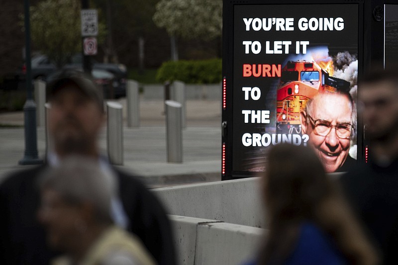 A truck with rotating images protesting over the ongoing contract negotiations for BNSF Railway union workers drives past people lining up for the Berkshire Hathaway 2022 Annual Shareholders Meeting outside the CHI Health Center in Omaha on Saturday, April 30, 2022. (Anna Reed/Omaha World-Herald via AP)