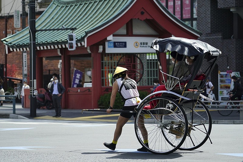FILE - A rickshaw puller carries tourists near Sensoji Buddhist temple at Tokyo's Asakusa district in Tokyo, March 31, 2021. Japan?s government announced Tuesday, May 17, 2022, it will begin allowing small package tours from four countries in later this month before gradually opening up to foreign tourism for the first time since it imposed tight border restrictions due to the coronavirus pandemic. (AP Photo/Eugene Hoshiko, File)