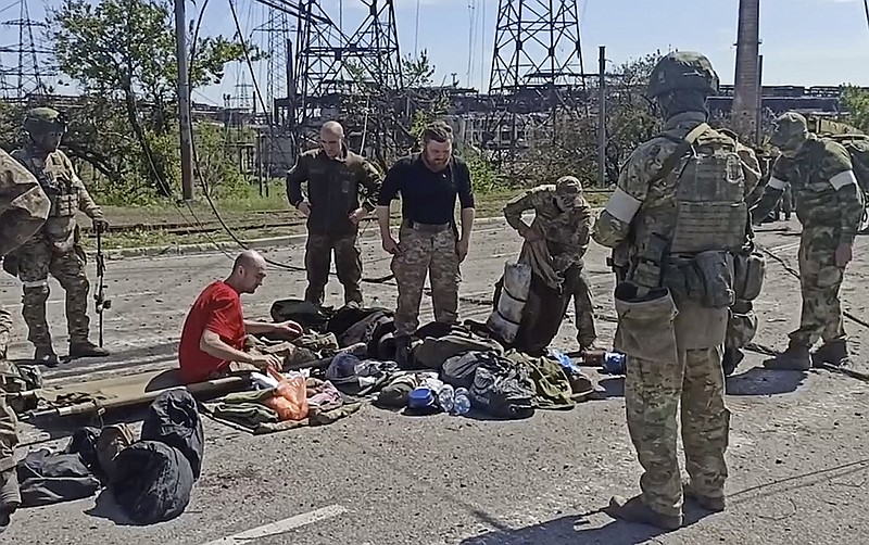 In this photo taken from video released by the Russian Defense Ministry Press Service on Wednesday, May 18, 2022, Russian servicemen frisk Ukrainian servicemen after they leaved the besieged Azovstal steel plant in Mariupol, Ukraine. (Russian Defense Ministry Press Service via AP)