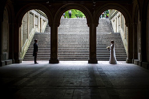 FILE - In this Tuesday, May 23, 2017 file photo, a bride and groom pose for wedding pictures at the Bethesda Terrace in New York's Central Park. Industry experts predict 2.5 million weddings in the U.S. this year, a 40-year high. That means millions of invited guests are weighing whether to attend — and how to cover costs if they do.   (AP Photo/Mary Altaffer, file)