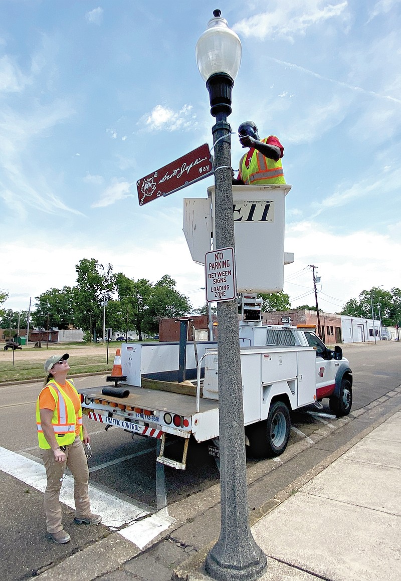 Public Works employee Eddie Jones, in the bucket lift, straightens the Scott Joplin sign on a light post outside City Hall on Wednesday, May 18, 2022, at Walnut and East Third streets in downtown Texarkana, Arkansas. Angel Hirschi, standing, said the Public Works department is planning other improvements around the municipal building, including a fresh coat of paint on the parking and traffic stripes. (Staff photo)