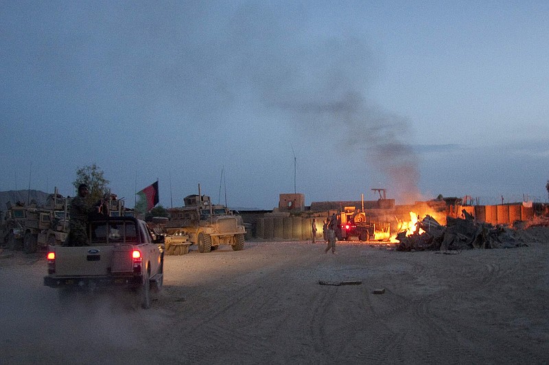 FILE - In this April 28, 2011, photo, an Afghan National Army pickup truck passes parked U.S. armored military vehicles, as smoke rises from a fire in a trash burn pit at Forward Operating Base Caferetta Nawzad, Helmand province south of Kabul, Afghanistan. (AP Photo/Simon Klingert, File)