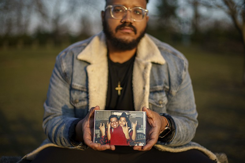 FILE - Adam Almonte holds a photo of him with his older brother, Fernando Morales, on a bench where they used to sit and eat tuna sandwiches after playing catch in Fort Tryon Park in New York, Wednesday, March 16, 2022. Morales died April 7, 2020 from COVID-19 at age 43. After a weekend of gun violence in America, Saturday, May 14, 2022,  when shootings killed and wounded people grocery shopping, going to church and simply living their lives, the nation marked a milestone of 1 million deaths from COVID-19. The number, once unthinkable, is now a pedestrian reality in the United States, just as is the reality of the continuing epidemic of gun violence that kills tens of thousands of people a year. (AP Photo/David Goldman, File)