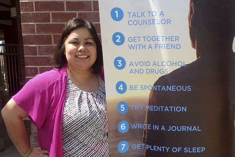 In this undated photo provided by Wendy Gonzalez, Alma Lopez, the district's school counselor coordinator and one of two counselors at Livingston Middle School, poses for a photo beside a mental health banner, in Livingston, Calif. At the school in rural central California, counselors have conducted suicide prevention lessons in classrooms for years. Pre-pandemic, the lessons would result in about 30 students saying they wanted to see a counselor, Lopez said. (Wendy Gonzalez via AP)