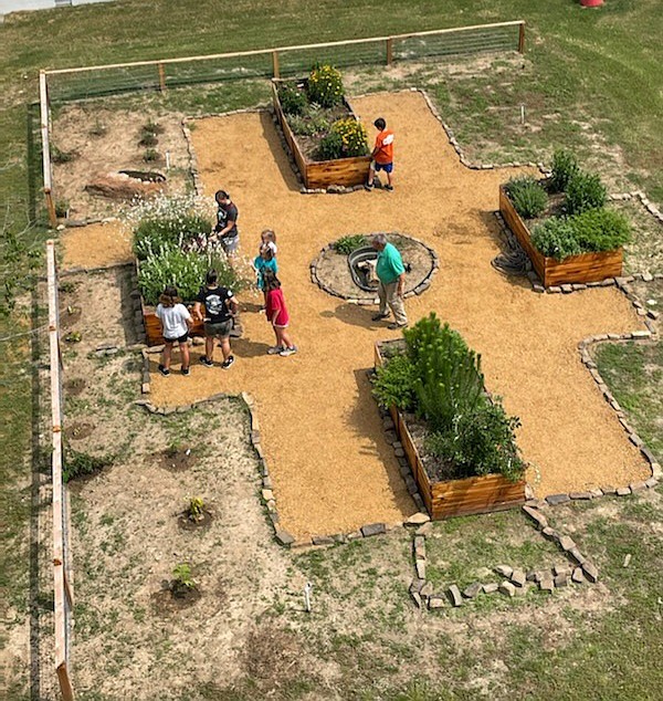 Members of Texarkana Arkansas Fire Department assist members of the Miller County Red Dirt Master Gardeners on Saturday, May 21, 2022, by using a ladder truck to take an aerial photo of the pollinator garden at the Gateway Farmers Market in Texarkana. The firefighters were at the  market for a barbecue lunch for first responders. Master Gardeners created the pollinator garden to attract bees and butterflies and to add a nature spot to the market. (Photo by Red Dirt Master Gardeners)