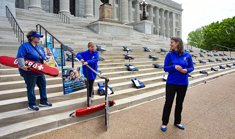 In recognition of Water Safety Month, members of the Missouri Alliance of YMCAs hosted a brief event on the Missouri Capitol steps Monday to bring attention to the issue. Kelly Schultz of the alliance joined YMCA lifeguard and swim instructor Lynn Schillers and Eleanor Hussey, a member of the YMCA Barracuda swim team, as they placed 46 lifejackets on the steps to represent the number of lives lost last year in non-boating incidents. (Julie Smith/News Tribune photo)