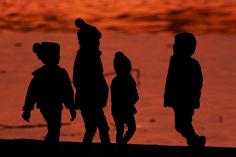 FILE - Kids are silhouetted against a pond at a park in Lenexa, Kan., on Saturday, Dec. 26, 2020. Health officials remain perplexed by mysterious cases of severe liver damage in hundreds of young children around the world. In May 2022, the U.S. Centers for Disease Control and Prevention officials said they are now looking into 180 possible cases across the U.S. More than 20 other countries have reported hundreds more cases in total, though the largest numbers have been in the U.K. and U.S. (AP Photo/Charlie Riedel, File)