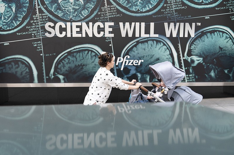 A woman pushes a baby in a stroller past a sign hanging outside Pfizer headquarters in New York, Monday, May 23, 2022. Three doses of Pfizer's COVID-19 vaccine offer strong protection for children younger than 5, the company announced Monday, May 23, 2022. Pfizer plans to give the data to U.S. regulators later this week in a step toward letting the littlest kids get the shots. (AP Photo/Mary Altaffer)