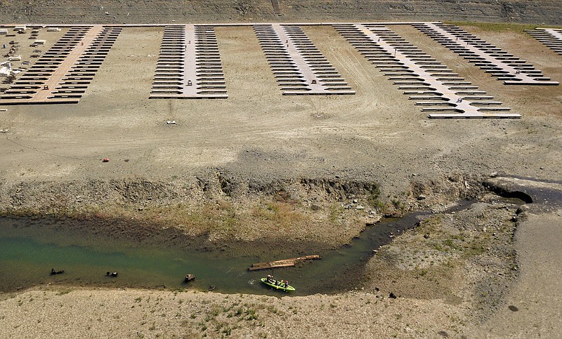 FILE - Kayakers navigate a narrow section of water near boat docks sitting on dry land at the Browns Ravine Cove area of drought-stricken Folsom Lake, in Folsom, Calif., Saturday, May 22, 2021. California Gov. Gavin Newsom threatened Monday, May 23, 2022, to impose mandatory, statewide restrictions on water use if people don't start using less on their own as the drought drags on and the hotter summer months approach. (AP Photo/Josh Edelson,File)