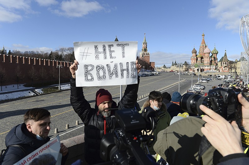 FILE - A man holds a poster with writing reading "No war" as people lay flowers near the site where Russian opposition leader Boris Nemtsov was gunned down, with the Kremlin Wall, left, the Spaskaya Tower, center, and St. Basil's in the background, in Moscow, Russia, Sunday, Feb. 27, 2022. (AP Photo, File)