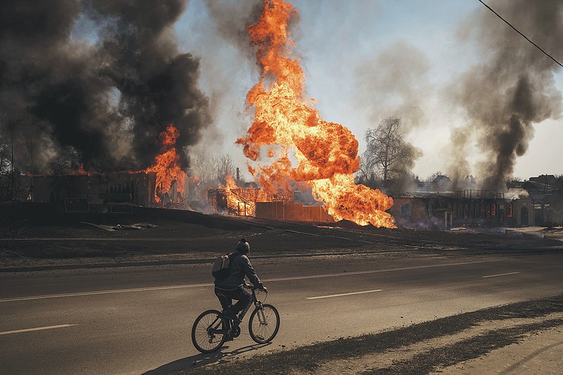 A man rides his bike past flames and smoke rising from a fire following a Russian attack in Kharkiv, Ukraine, Friday, March 25, 2022. (AP Photo/Felipe Dana)