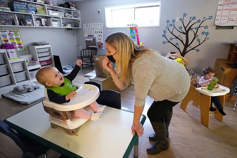 FILE - Amy McCoy signs to a baby about food as a toddler finishes lunch behind at her Forever Young Daycare facility, Monday, Oct. 25, 2021, in Mountlake Terrace, Wash. According to a report released by the Centers for Disease Control and Prevention on Tuesday, May 24, 2022, U.S. births bumped up in 2021, but the number of babies born was still lower than before the coronavirus pandemic. (AP Photo/Elaine Thompson, File)