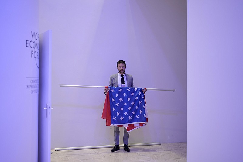 A man waits at the stage entrance with flags of China and The United States ahead a climate panel during the World Economic Forum in Davos, Switzerland, Tuesday, May 24, 2022. The annual meeting of the World Economic Forum is taking place in Davos from May 22 until May 26, 2022. (AP Photo/Markus Schreiber)