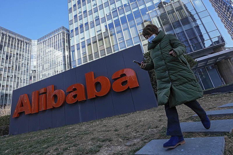 FILE - A woman wearing a face mask run past the offices of Chinese e-commerce firm Alibaba in Beijing on Dec. 13, 2021.   Alibaba Group Holding Ltd on Thursday, May 26, 2022, reported a single-digit increase in its fourth-quarter revenue, its slowest quarter yet as its online services and e-commerce businesses took a hit amid COVID-19 lockdowns across China. (AP Photo/Andy Wong, File)