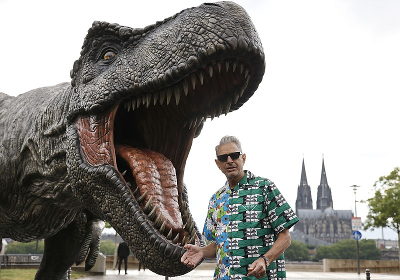 Actor Jeff Goldblum stands in front of a T-Rex figure, with the Cologne Cathedral in the background, during a photocall for the new film - Jurassic World Dominion, in Cologne, Germany, Sunday, May 29, 2022.  (Thomas Banneyer/dpa via AP)