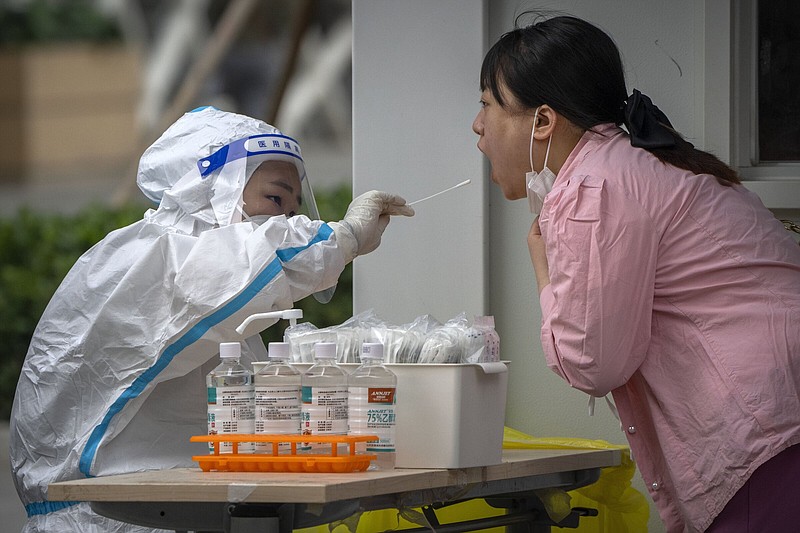 A worker wearing a protective suit swabs a woman's throat for a COVID-19 test at a coronavirus testing site in Beijing, Thursday, June 9, 2022. Thousands of COVID-19 testing booths have popped up on sidewalks across Beijing and other Chinese cities in the latest twist to the country's "zero-COVID" strategy. (AP Photo/Mark Schiefelbein)