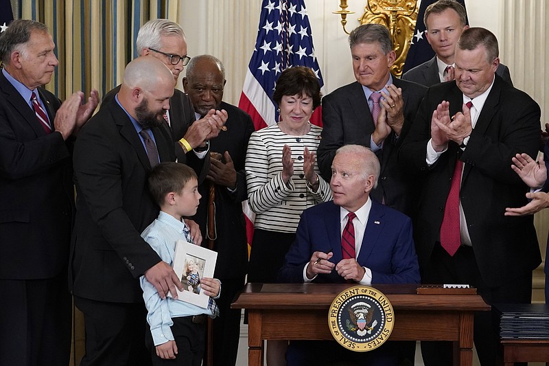 President Joe Biden, seated, looks at Shane Thomas, second from left, husband of the late Marine Corps veteran Kate Hendricks, after signing a bill named after her during an event in the State Dining Room of the White House in Washington, Tuesday, June 7, 2022. Her son Matthew also attends. (AP Photo/Susan Walsh)