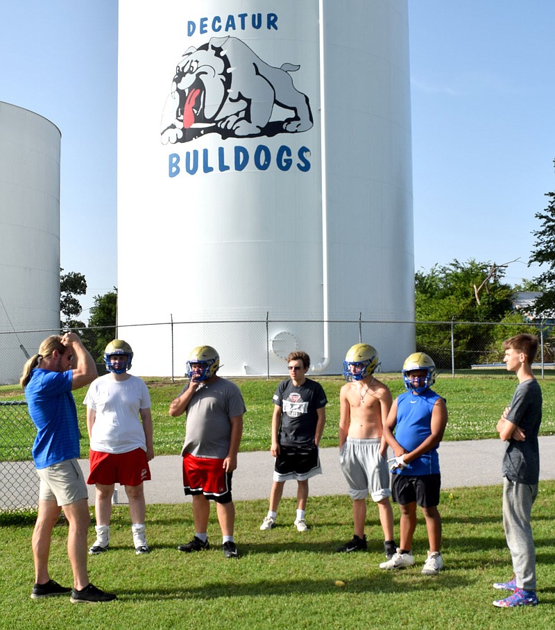 Westside Eagle Observer/MIKE ECKELS
With the Decatur Bulldog water tower serving as a backdrop, football coach Jake Denzer (left) talks to a small group of junior and senior high football players about the upcoming football camp in Berryville. Both Bulldog teams had a light off-season practice session at Bulldog Stadium in Decatur June 14.