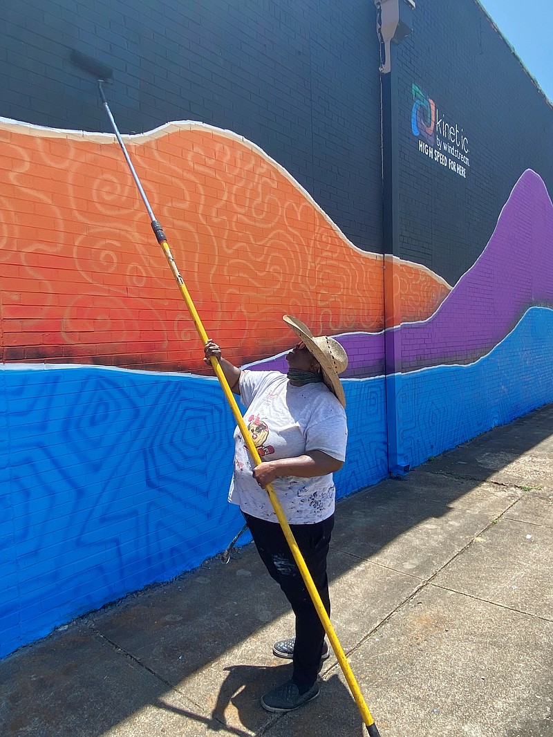 Local muralist Darlene Taylor touches up the background color Thursday, June 16, 2022, on a new downtown mural at West Third Street and Texas Boulevard. The mural will feature a stylized rendering of the word "here" that will incorporate elements of the Twin Cities' culture. (Staff photo)