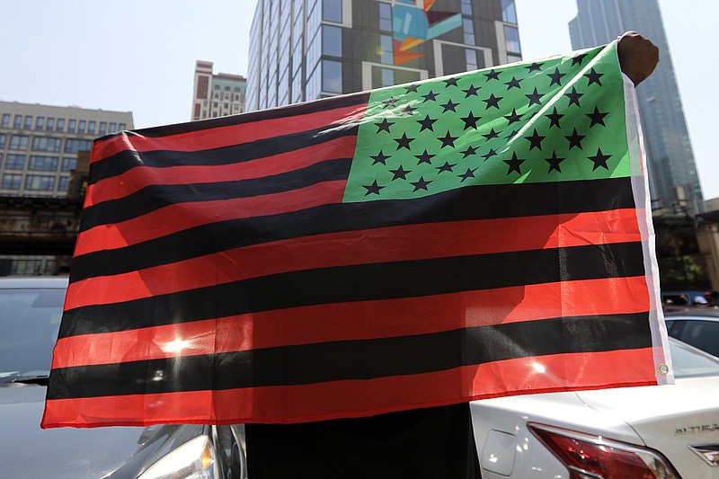 FILE - A man holds an African-American flag during a demonstration in Chicago on June 19, 2020, to mark Juneteenth, the holiday celebrating the day in 1865 that enslaved black people in Galveston, Texas, learned they had been freed from bondage, more than two years after the Emancipation Proclamation. Retailers and marketers from Walmart to Amazon have been quick to commemorate Juneteenth with an avalanche of merchandise from ice cream to T-shirts to party favors. (AP Photo/Nam Y. Huh, File)