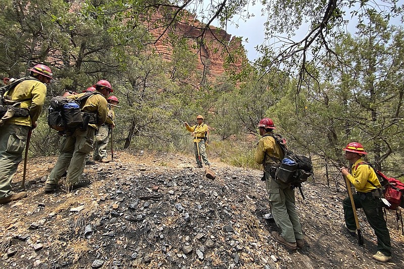 In this photo provided by the U.S. Forest Service, Jason Nez, center, talks to wildland fire personnel working a blaze in northern Arizona in 2021. Nez is a Navajo archaeologist and firefighter who advises fire officials on how to protect archaeological resources. (Paul Dawson/U.S. Forest Service via AP)