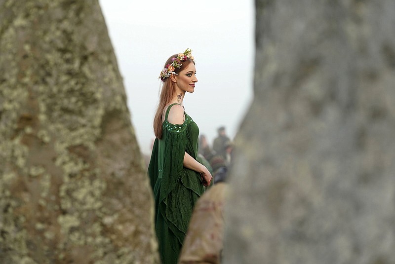 A woman dressed in pagan attire watches the sun rise during the Summer Solstice festivities at Stonehenge in Wiltshire, England, Tuesday, June 21, 2022. After two years of closure due to the COVID-19 pandemic, Stonehenge reopened Monday for the Summer Solstice celebrations. (Andrew Matthews/PA via AP)