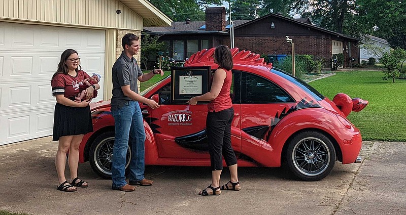 Dakotah Cooper is presented with his diploma by Megan Whobrey, adviser and academic services coordinator in the College of Engineering at the University of Arkansas while his wife Natalie Cooper and daughter Piper watched. (Joshua Turner/Banner News)