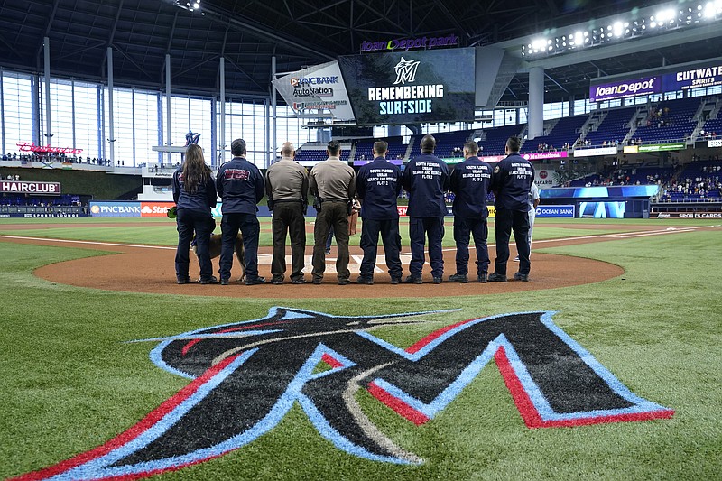 A South Florida Urban Search and Rescue Team stands for a moment of silence to remember the victims of the Surfside building collapse, before a baseball game between the Miami Marlins and the New York Mets, Friday, June 24, 2022, in Miami. (AP Photo/Lynne Sladky)