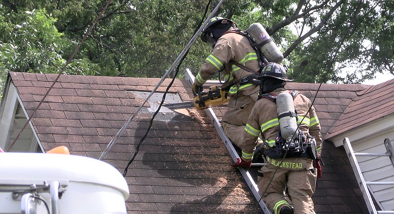 Two Hot Springs firefighters cut through the roof of a residence in the 100 block of Kenwood Street, just off Maryland Street, to vent a fire that started shortly after 3:30 p.m. Monday. - Photo by Donald Cross of the Sentinel-Record