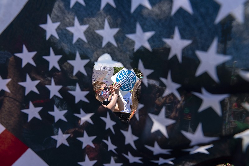 Activistas a favor del aborto vistos a través de un agujero en una bandera de EEUU durante una manifestación frente a la Corte Suprema en Washington el 25 de junio del 2022.  (AP Photo/José Luis Magaña)