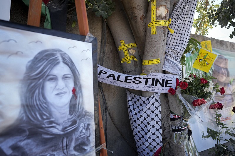 Yellow tape marks bullet holes on a tree and a portrait and flowers create a makeshift memorial on o May 19, 2022, at the site where Palestinian-American Al-Jazeera journalist Shireen Abu Akleh was shot and killed in the West Bank city of Jenin. The Palestinian Authority on Saturday, July 2, 2022, said it has given the bullet that killed Al Jazeera journalist Shireen Abu Akleh to American forensic experts, taking a step toward resolving a standoff with Israel over the investigation into her death. (AP Photo/Majdi Mohammed)