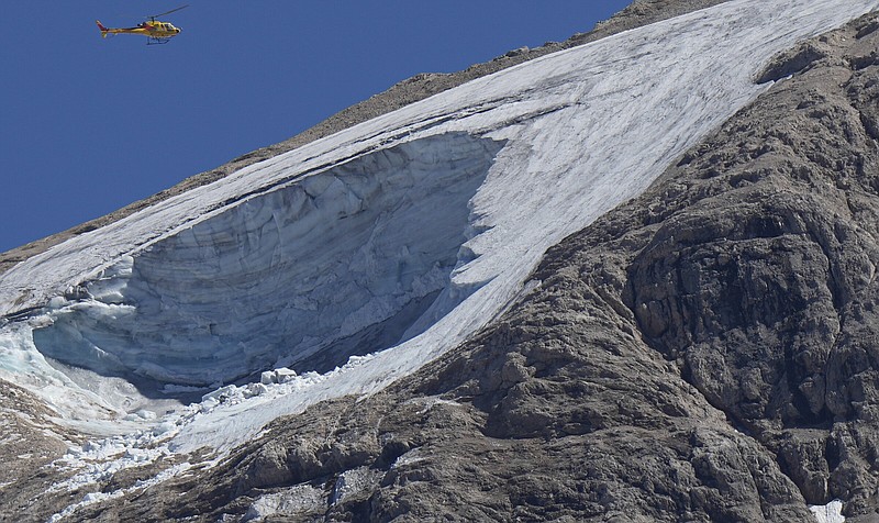 A rescue helicopter hovers over the Punta Rocca glacier near Canazei, in the Italian Alps in northern Italy, Monday, July 4, 2022, a day after a huge chunk of the glacier broke loose, sending an avalanche of ice, snow, and rocks onto hikers. Rescuers said conditions downslope from the glacier, which has been melting for decades, were still too unstable to immediately send rescuers and dogs into the area to look for others buried under tons of debris. (AP Photo/Luca Bruno)