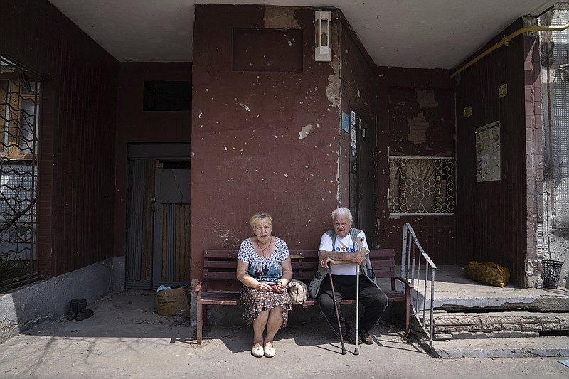 Pavel Govoryhov, 84, and Tatiana Koneva, 75, residents of Saltivka district, sit on a bench in front of their apartment house in Kharkiv, Ukraine, Tuesday, July 5, 2022. (AP Photo/Evgeniy Maloletka)