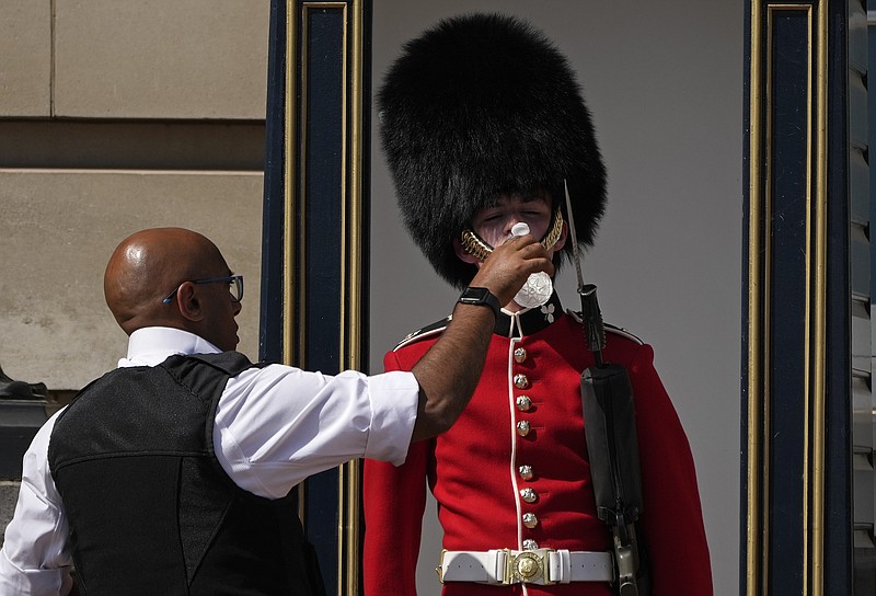 Un policía da agua a un soldado británico que monta guardia afuera del Palacio de Buckingham, el lunes 18 de julio de 2022, en Londres. (AP Foto/Matt Dunham)