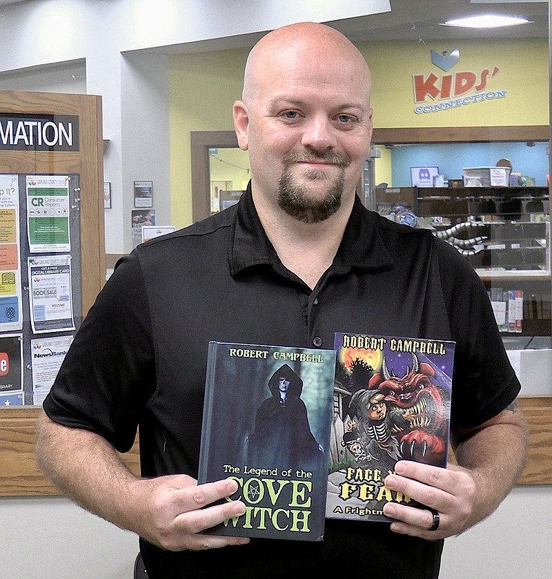 Hot Springs-based author Robert Dustin Campbell recently holds up two of his published books inside the Garland County Library. He is currently working on two others he hopes to have out soon. - Photo by Donald Cross of The Sentinel-Record