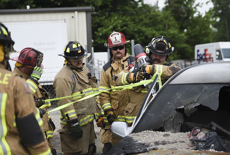 Captain Bryan Gallogly (center) observes as firefighter Joey Donaldson (right) uses a spreader to remove the door from a car June 28 during a firefighter training in Bentonville. 
(NWA Democrat-Gazette/Charlie Kaijo)