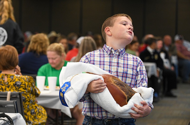 Julie Smith/News Tribune
After making several passes while carrying his ham, Emmett Rackers said "this is getting really heavy" as the final bids were cast so he made his way to the table to set it down. Rackers, a member of St. Thomas 4-H Club, ventured for the first time into curing a ham and showing it during Friday's Cole County Fair 4-H and FFA Ham and Bacon Auction at Farm Bureau Heaequarters.
