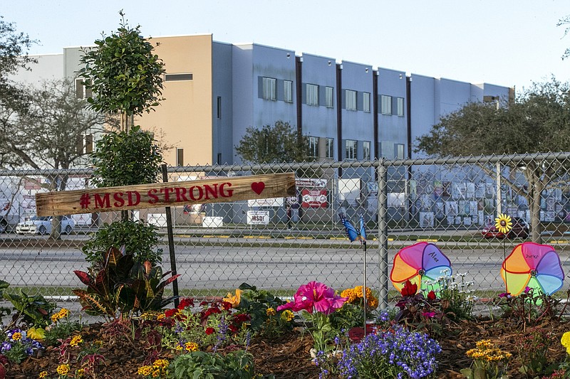 A memorial to the victims is seen outside Marjory Stoneman Douglas High School in Parkland, Fla., during the one-year anniversary of the school shooting, Thursday, Feb. 14, 2019. The three story building in the background is where the massacre happened. Jurors in the trial of Florida school shooter Nikolas Cruz are expected to walk through the still blood-spattered rooms of the high school Thursday, Aug. 4, 2022, in a visit to the three-story building where he murdered 14 students and three staff members four years ago. (Al Diaz/Miami Herald via AP, File)