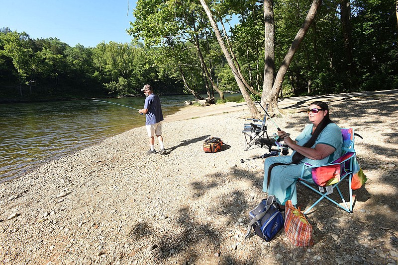 Flip Putthoff/NWA Democrat Gazette Rene Hager of Fayetteville has it made in the shade while she and her husband, Dave Hager, fish for trout near the cold water of the White River below Beaver Dam on July 1. Water temperature in the river is around 55 degrees in the heat of summer and most of the year.