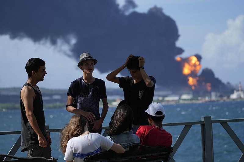 Youth gather on a dock while flames and smoke continue to rise from the Matanzas Supertanker Base, as firefighters and specialists work to quell the blaze which began during a thunderstorm the night before, in Matazanas, Cuba, Saturday, Aug. 6, 2022. Cuban authorities say lightning struck a crude oil storage tank at the base, causing a fire that led to four explosions which injured dozens. (AP Photo/Ramon Espinosa)