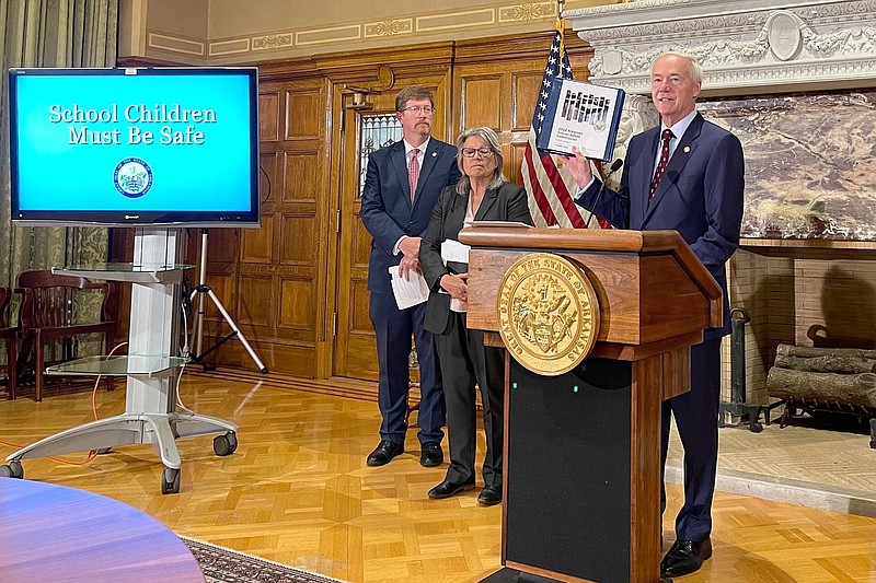 Arkansas Gov. Asa Hutchinson holds up an interim report from a commission formed to review school safety measures at a news conference at the state Capitol in Little Rock, Arkansas, on Tuesday, Aug. 2,2022. A proposed $50 million grant program for school safety is on the agenda for a legislative special session that is being held this week. (AP Photo/Andrew DeMillo)