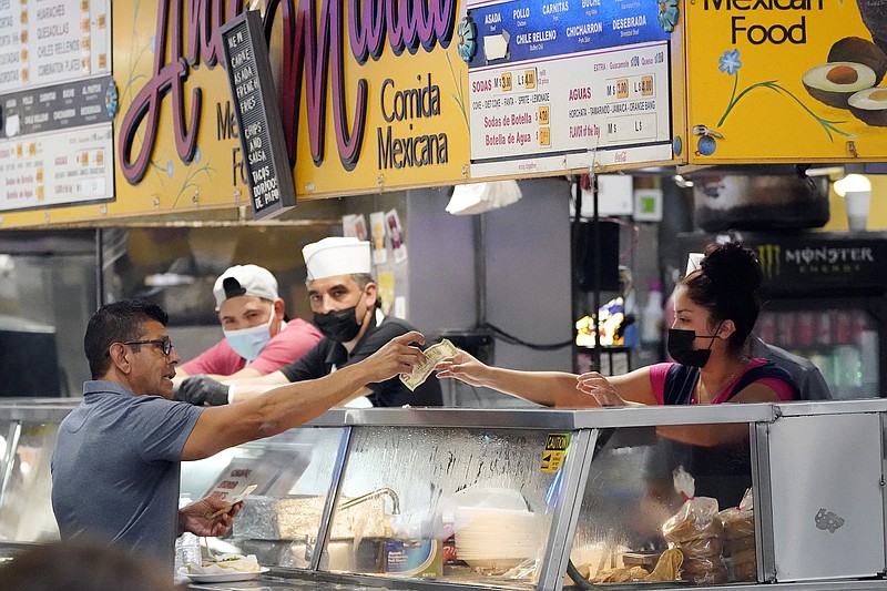 Money is exchanged at a food stand while workers wear face masks inside Grand Central Market on Wednesday, July 13, 2022, in Los Angeles. Falling gas prices gave Americans a slight break from the pain of high inflation last month, though the surge in overall prices slowed only modestly from the four-decade high it reached in June. And even as gas prices fall, inflation in services such as health care, rents and restaurant meals is accelerating. (AP Photo/Marcio Jose Sanchez)