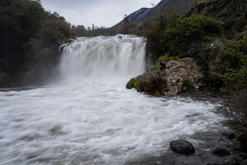 Ruben Onate takes pictures sitting next to the largest waterfall of the Truful Truful River, near Melipeuco, southern Chile, on Thursday, June 30, 2022. Mapuche people believe in the falling water's distinctive &quot;energy power&quot; for healing purposes, either in riverside ceremonies or by taking large soda bottles full of it back home. (AP Photo/Rodrigo Abd)