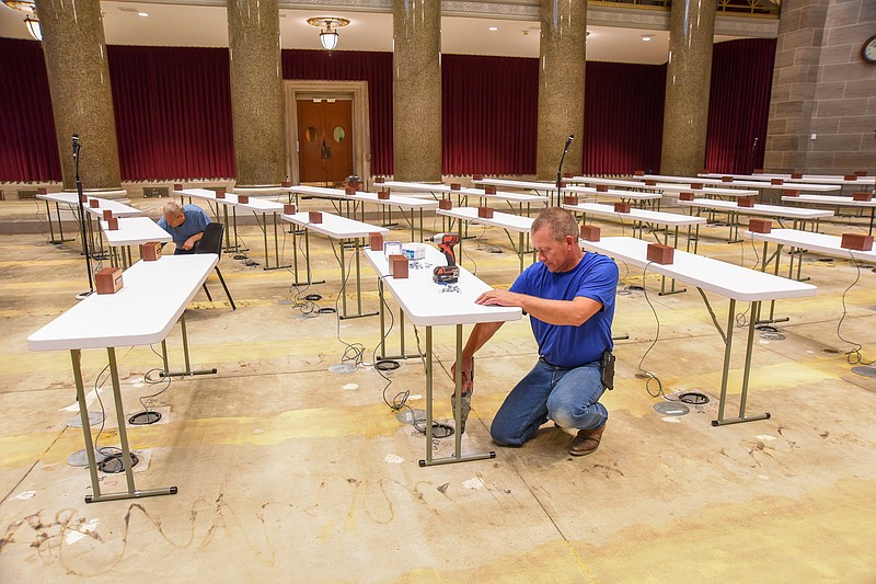 Russ Alberts drills holes in the concrete in order to fasten a clamp to the feet of the desks that have temporarily been set up in the Missouri House of Representatives for the beginning of a special session. The chamber is undergoing a major renovation so temporary accommodations have been made so legislators have a place from which to work while in session. Working in the background is Craig Reinkemeyer who typically works in the House post office but is helping out with the project so it can be ready when the bell rings Tuesday, Sept. 6, 2022. (Julie Smith/News Tribune photo)