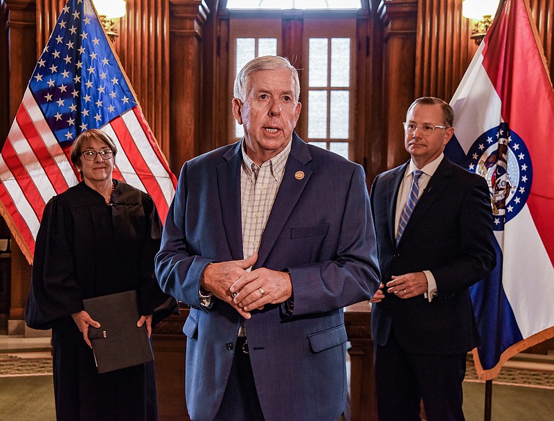 As Judge Patricia Breckenridge, at left, waits to swear in Brian Treece, background right, as the newest commissioner of the Missouri Highways and Transportation Commission, Gov. Mike Parson delivers a few comments about why Treece was appointed to the position. Treece was sworn in during a brief ceremony Tuesday, Sept. 6, 2022, in Parson's Capitol office. (Julie Smith/News Tribune photo)