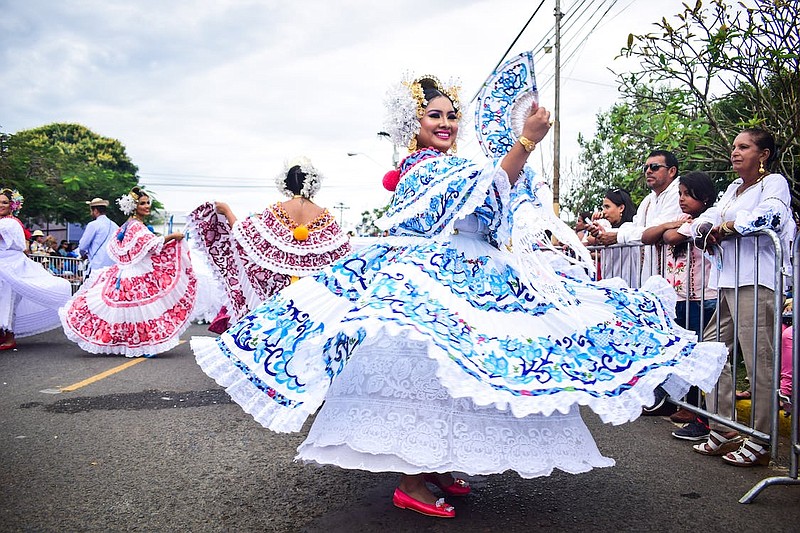 Dos mujeres en vestido rojo y blanco de pie sobre la carretera de asfalto sondeando sus vestidos folclóricos. Créditos: Caleb Jiménez.
