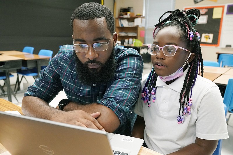 Ryan Johnson, a fifth-grade teacher at Pecan Park Elementary School, left, checks to see what homework daughter Ryeli is taking home as they prepare to leave Johnson's classroom Tuesday, Sept. 6, 2022, in Jackson, Miss. Because the city's long-standing water issues recently forced the public schools to again revert to remote learning, Johnson brought his daughter to work where she could be monitored as she also attended virtual classes, while he taught his students virtually. (AP Photo/Rogelio V. Solis)